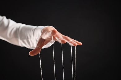 Woman pulling strings of puppet on black background, closeup