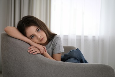 Sad little girl sitting on sofa indoors, space for text