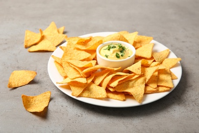 Plate with delicious mexican nachos chips and cheese sauce on grey table