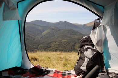 Camping tent with backpack and thermos in mountains on sunny day, view from inside