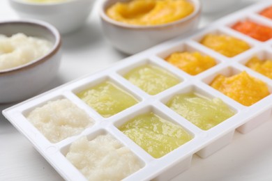 Different purees in ice cube tray and bowls on white table, closeup. Ready for freezing