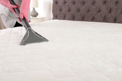 Woman disinfecting mattress with vacuum cleaner, closeup. Space for text