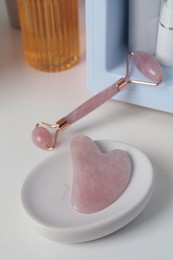 Photo of Rose quartz gua sha tool, natural face roller and cosmetic products on white table