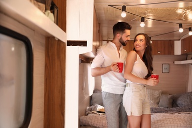 Happy young couple with cups in trailer. Camping vacation