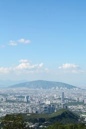 Picturesque view of city with trees, mountains and buildings under beautiful sky