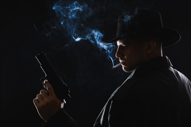 Old fashioned detective with gun smoking cigarette on dark background