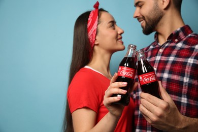 MYKOLAIV, UKRAINE - JANUARY 27, 2021: Young couple holding bottles of Coca-Cola against light blue background, closeup. Space for text