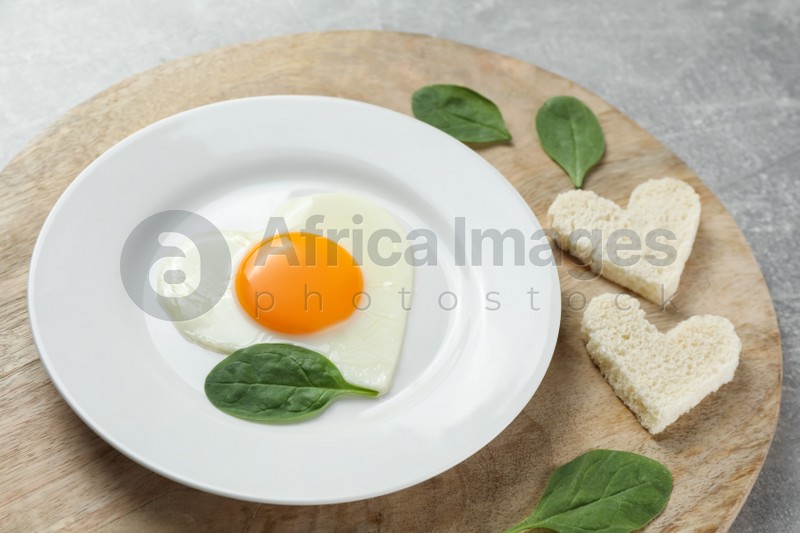 Romantic breakfast with heart shaped fried egg and toasts on light grey table, closeup