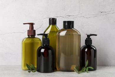 Photo of Shampoo bottles and leaves on light grey table