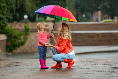 Happy mother and daughter with bright umbrella under rain outdoors