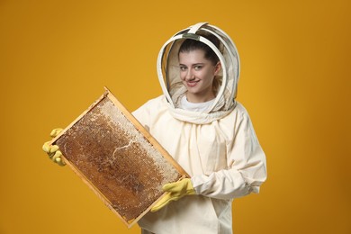 Photo of Beekeeper in uniform holding hive frame with honeycomb on yellow background