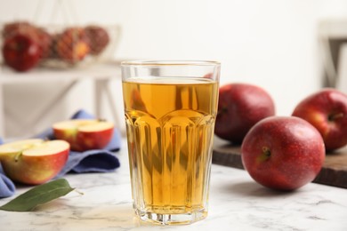 Glass of delicious cider and ripe red apples on white marble table