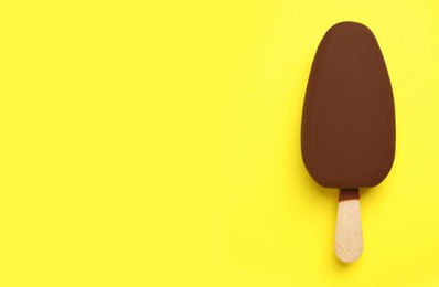 Ice cream glazed in chocolate on yellow background, top view. Space for text