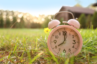 Photo of Pink alarm clock on green grass outdoors. Space for text