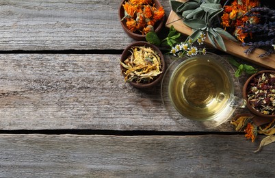 Glass cup of aromatic freshly brewed tea near different dry herbs on wooden table, flat lay. Space for text