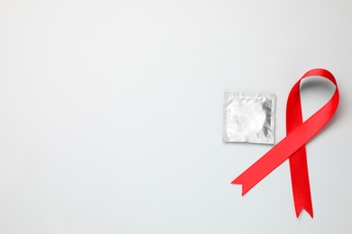 Red ribbon and condom on white background, top view. AIDS disease awareness