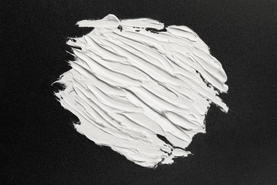 Strokes of white oil paint on black canvas, top view