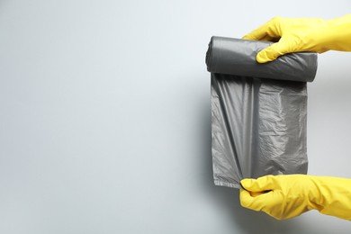 Janitor in rubber gloves holding roll of grey garbage bags over light background, top view. Space for text