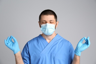 Doctor in protective mask meditating on grey background. Dealing with stress caused by COVID‑19 pandemic