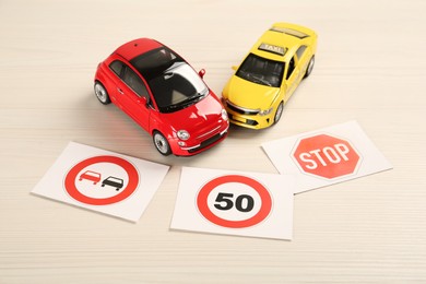 Cards with different road signs and toy cars on white wooden table. Driving school