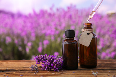Dripping essential oil from pipette into bottle near lavender flowers on wooden table, closeup. Space for text