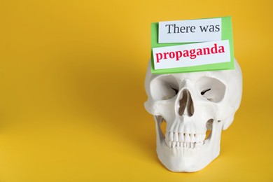 Photo of Information warfare concept. Human skull and paper cards with phrase There Was Propaganda on yellow background, space for text