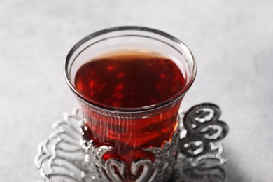 Photo of Glass of traditional Turkish tea in vintage holder on light grey table, closeup