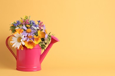 Pink watering can with beautiful flowers on yellow background, space for text