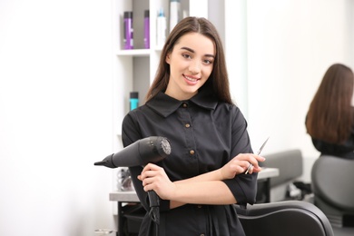 Professional female hairdresser with dryer and scissors in salon