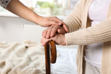 Caregiver and elderly woman with walking cane at home, closeup