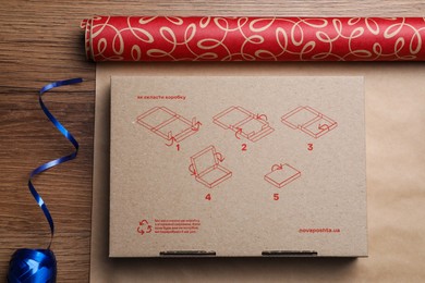 Roll of wrapping paper, gift box and ribbon on wooden table, flat lay