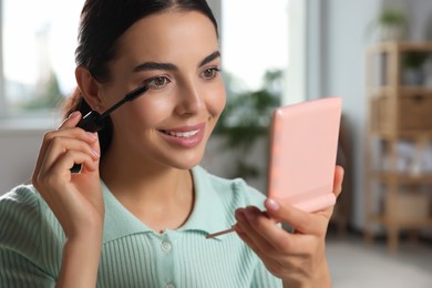 Photo of Young woman using cosmetic pocket mirror while applying make up indoors