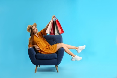Beautiful young woman with paper shopping bags in armchair on light blue background