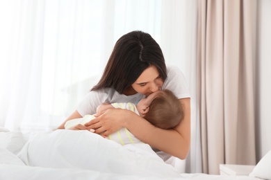 Mother with her adorable baby sitting on bed indoors