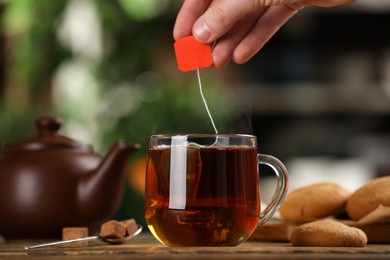 Man taking tea bag out of cup with beverage at wooden table, closeup