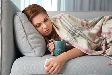 Sick woman with cup of hot drink lying on sofa at home. Influenza virus