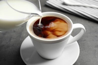 Pouring milk into cup of hot coffee on grey table, closeup