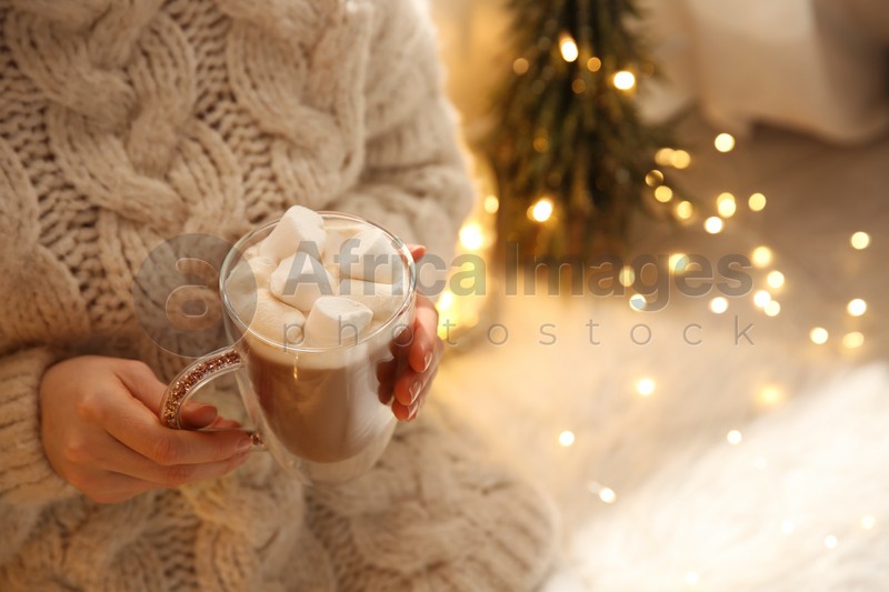 Woman holding cup of hot drink with marshmallow indoors, closeup