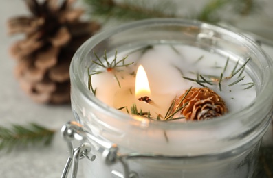 Burning scented conifer candle in glass jar, closeup view