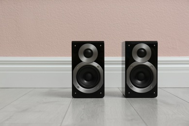 Modern powerful audio speakers on floor near pink wall