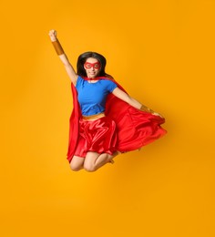 Confident young woman in superhero costume jumping on orange background