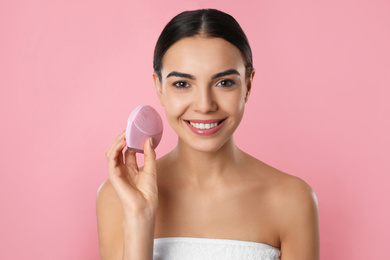 Young woman holding facial cleansing brush on pink background. Washing accessory