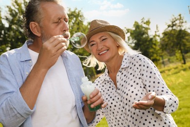 Lovely mature couple spending time together in park. Man blowing soap bubbles