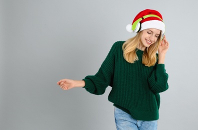 Happy woman with headphones on grey background, space for text. Christmas music
