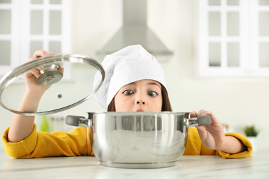 Surprised little girl wearing chef hat with pot in kitchen