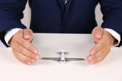 Insurance agent covering toy plane at table, closeup. Travel safety concept