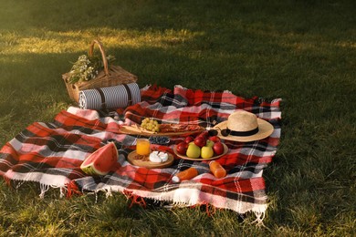 Picnic basket, food and drinks on plaid outdoors