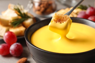 Dipping piece of bread into tasty cheese fondue at table, closeup