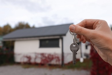 Photo of Real estate agent holding keys to new house outdoors, closeup. Space for text