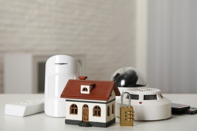 House model, CCTV camera, remote control, lock, smoke and movement detectors on table in room. Home security system